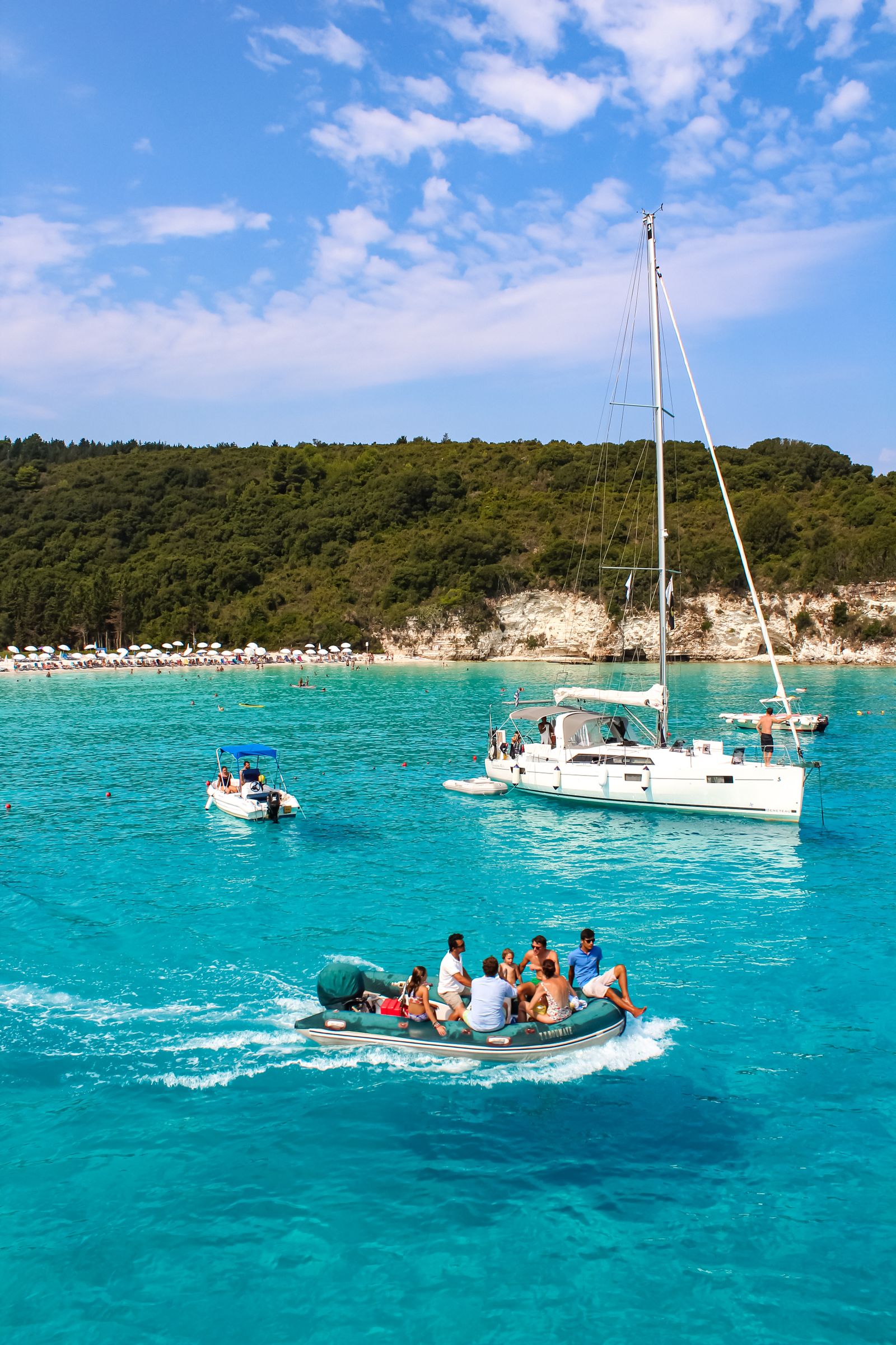 Sailboat anchored in turquoise water off a green Ionian island shore