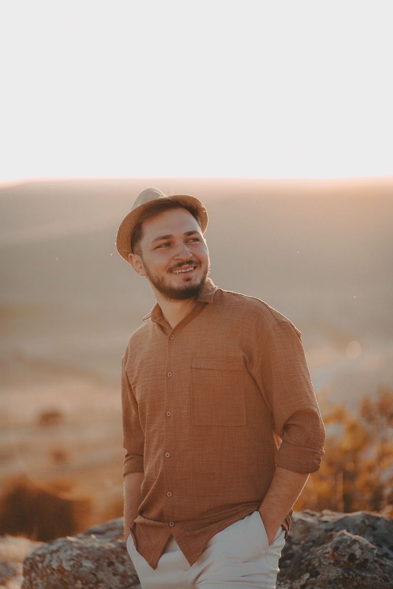 Young man in a fedora and casual shirt smiling in warm sunset light