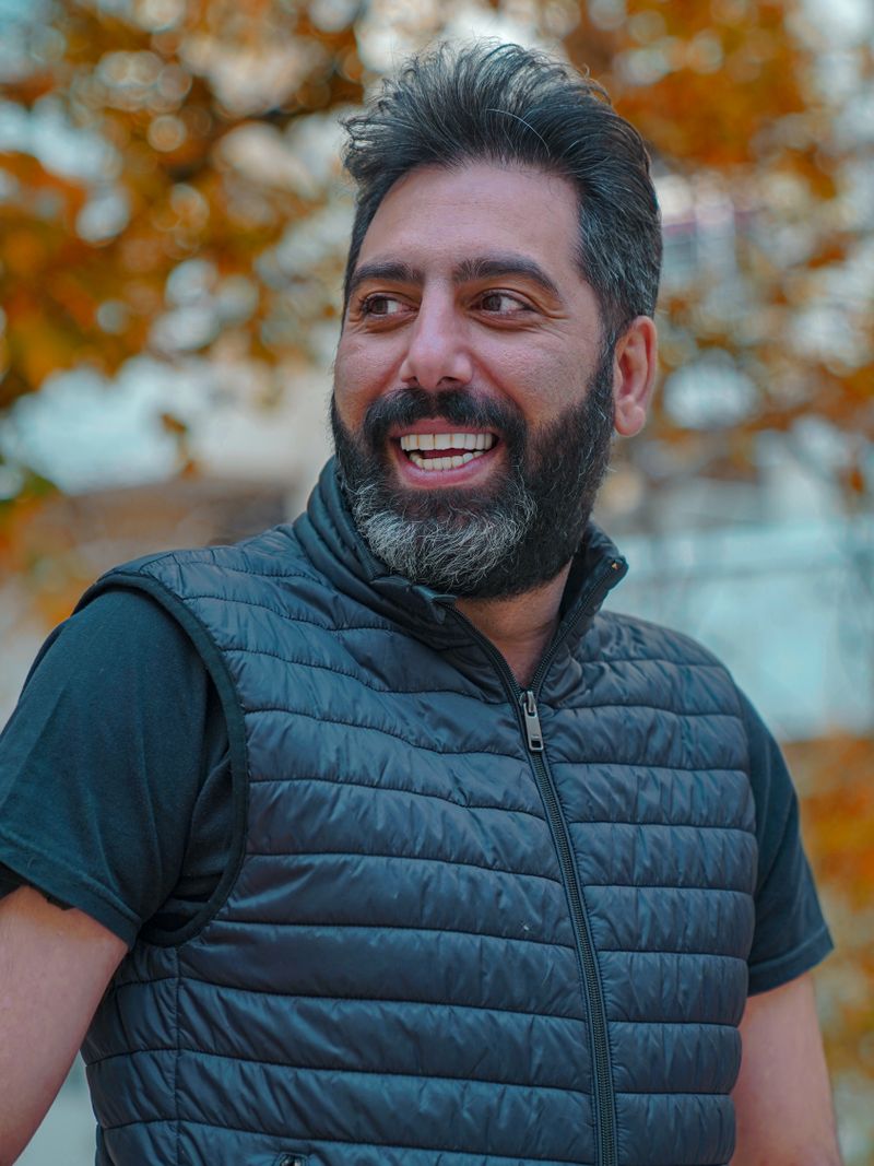 Smiling bearded man outdoors in a quilted vest with autumn foliage