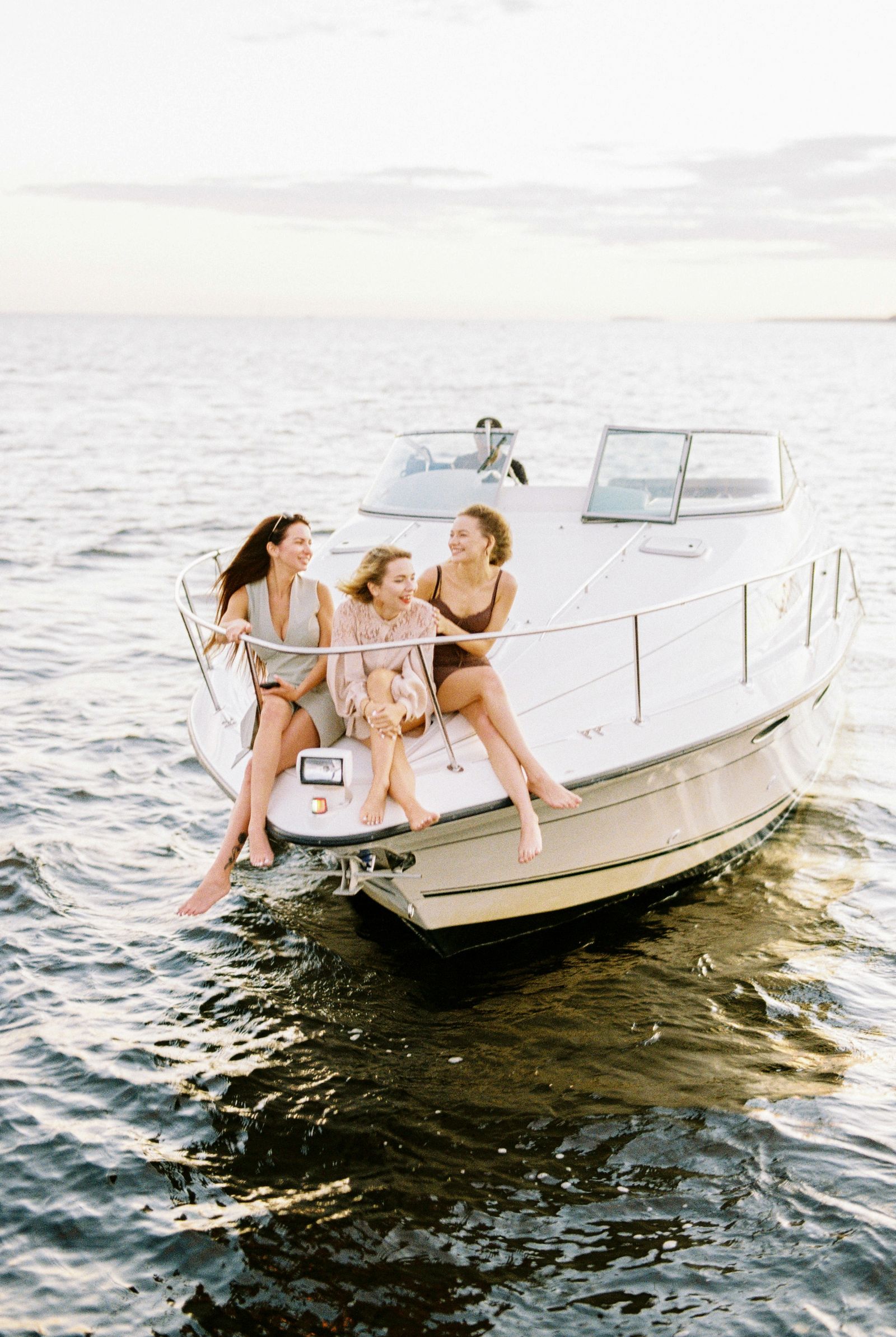 Three friends sitting together on the bow of a boat at sea, smiling